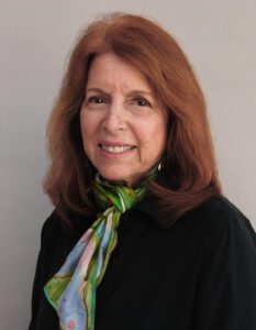 Smiling woman with red hair wearing a colorful scarf and black top.