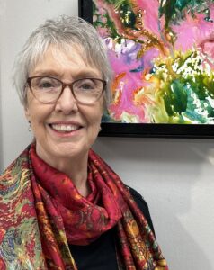 Smiling woman with glasses and colorful scarf in front of vibrant abstract art.
