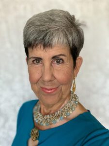Portrait of a confident older woman with silver hair and elegant jewelry.