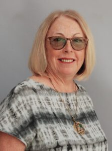Smiling woman with glasses and blonde hair wearing a patterned top.