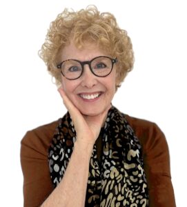 Smiling woman with curly hair and glasses wearing a scarf.