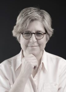 Professional portrait of a thoughtful mature woman with glasses and gray hair.