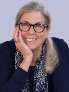 Smiling woman with glasses resting her face on her hand.