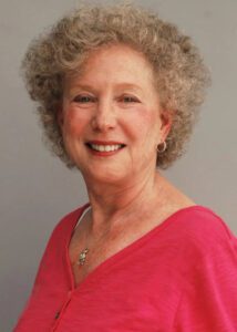 Smiling elderly woman with curly gray hair in a pink top.