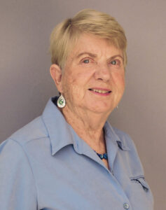 Portrait of an elderly woman with short blonde hair and blue shirt.
