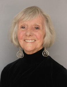 Smiling elderly woman with white hair and round earrings.