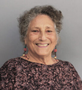 Smiling elderly woman with curly gray hair and colorful earrings.