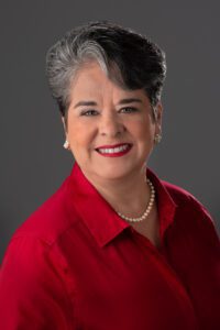 Smiling woman with gray hair wearing a red top and pearl necklace.