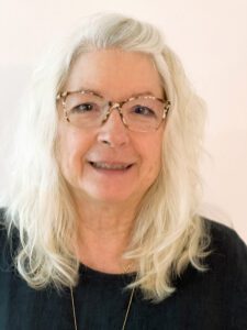 Smiling older woman with long white hair and glasses.