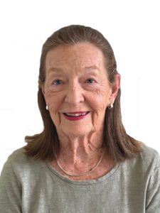 Smiling elderly woman with shoulder-length brown hair against white background.