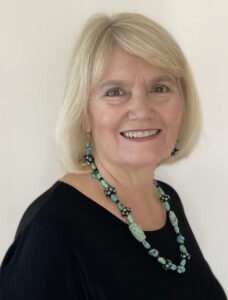 Smiling woman with blonde hair wearing a black top and turquoise necklace.