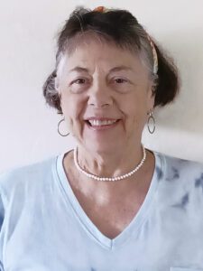 Smiling elderly woman with short hair and pearl necklace.
