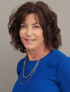 Portrait of a smiling woman with curly brown hair wearing a blue top.