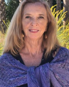 Smiling woman wrapped in a purple shawl outdoors in natural light.