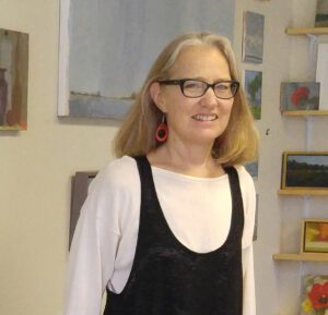Smiling woman wearing glasses indoors with artwork in the background.