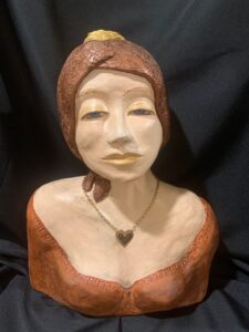 Carved wooden bust of a woman wearing a headscarf and necklace.