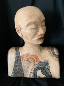 A sculpture of a bald person with closed eyes and detailed tattoos on their chest and shoulders.