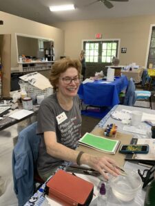A woman smiling while working with art supplies in a cozy room.