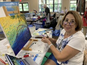 Woman painting a colorful landscape in a bright art studio.