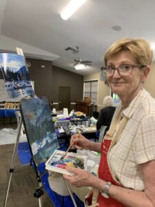 Woman painting a landscape on canvas in a cozy room.