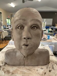 A clay bust sculpture with a surprised facial expression.