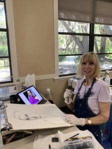 Woman painting in a sunlit art studio with digital reference.