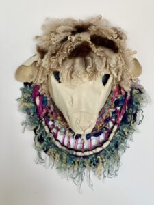 A unique sheep skull mask adorned with colorful yarn and fabric.