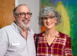 Smiling older couple posing in front of colorful artwork.