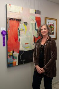 Woman standing next to a colorful abstract painting with a purple ribbon.