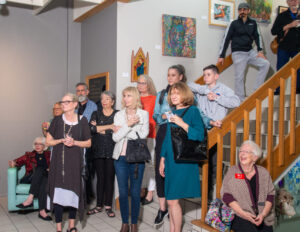 A group of people gathered indoors, some standing and some sitting, attentively listening.