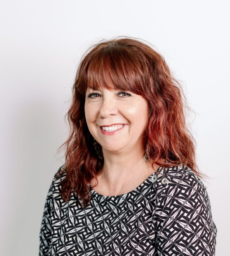Smiling woman with red hair and patterned blouse against a white background.