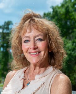 Smiling woman with curly hair outdoors on a sunny day.
