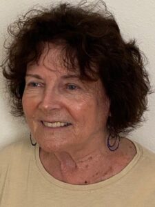 Smiling elderly woman with curly hair in a beige top.
