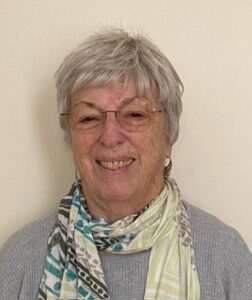 Smiling elderly woman wearing glasses and a patterned scarf.