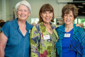 Three smiling older women posing together indoors.