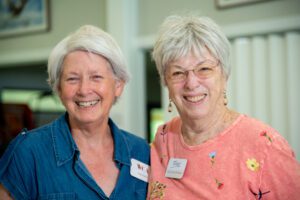 Two elderly women smiling warmly at the camera indoors.