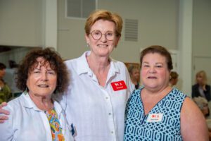 Three smiling women wearing name tags at a social event.