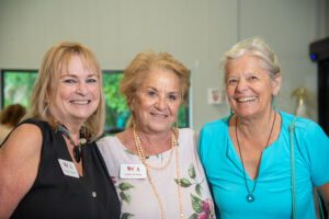 Three smiling older women posing together indoors.