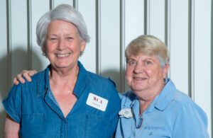 Two elderly women smiling, wearing blue shirts and name tags.