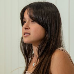 Young woman with long dark hair looking to the side indoors.