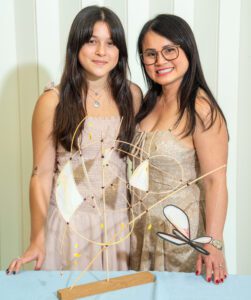 Two smiling women posing with a decorative art piece indoors.