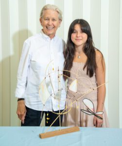 An elderly man and a young woman smiling beside a wire sculpture.
