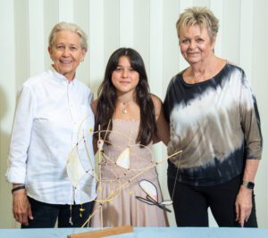 Three women smiling together indoors, dressed casually.