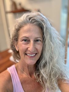 Smiling woman with long curly gray hair wearing a pink tank top.