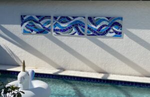 Decorative blue mosaic tiles above a sunlit swimming pool casting shadows.