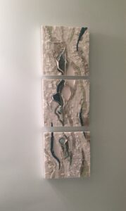 Three abstract textured art pieces in neutral tones arranged vertically on a wall.
