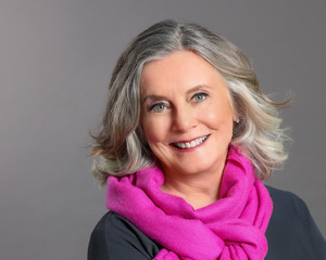 Smiling middle-aged woman with gray hair and a vibrant pink scarf.