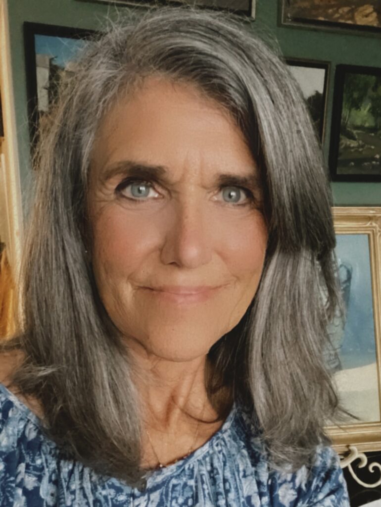 Close-up portrait of a woman with long gray hair and blue eyes.