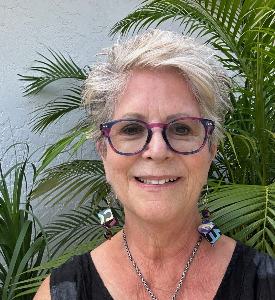 Smiling woman with short gray hair and glasses outdoors.