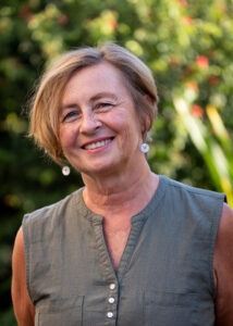 Smiling older woman outdoors with short blonde hair and pearl earrings.